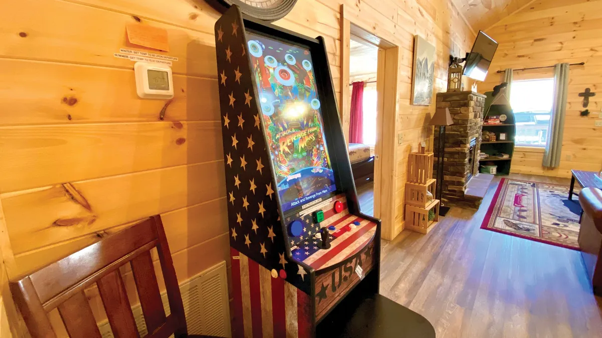 A fun, family-friendly game area with an arcade game machine, cozy wooden walls, a fireplace, and comfortable seating. The ambiance is playful yet relaxed, blending entertainment with comfort.