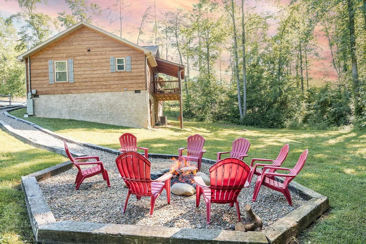 A cozy fire pit encircled by red chairs, with the house visible in the background. The scene conjures images of communal campfire gatherings, relaxation, and stargazing after dusk.