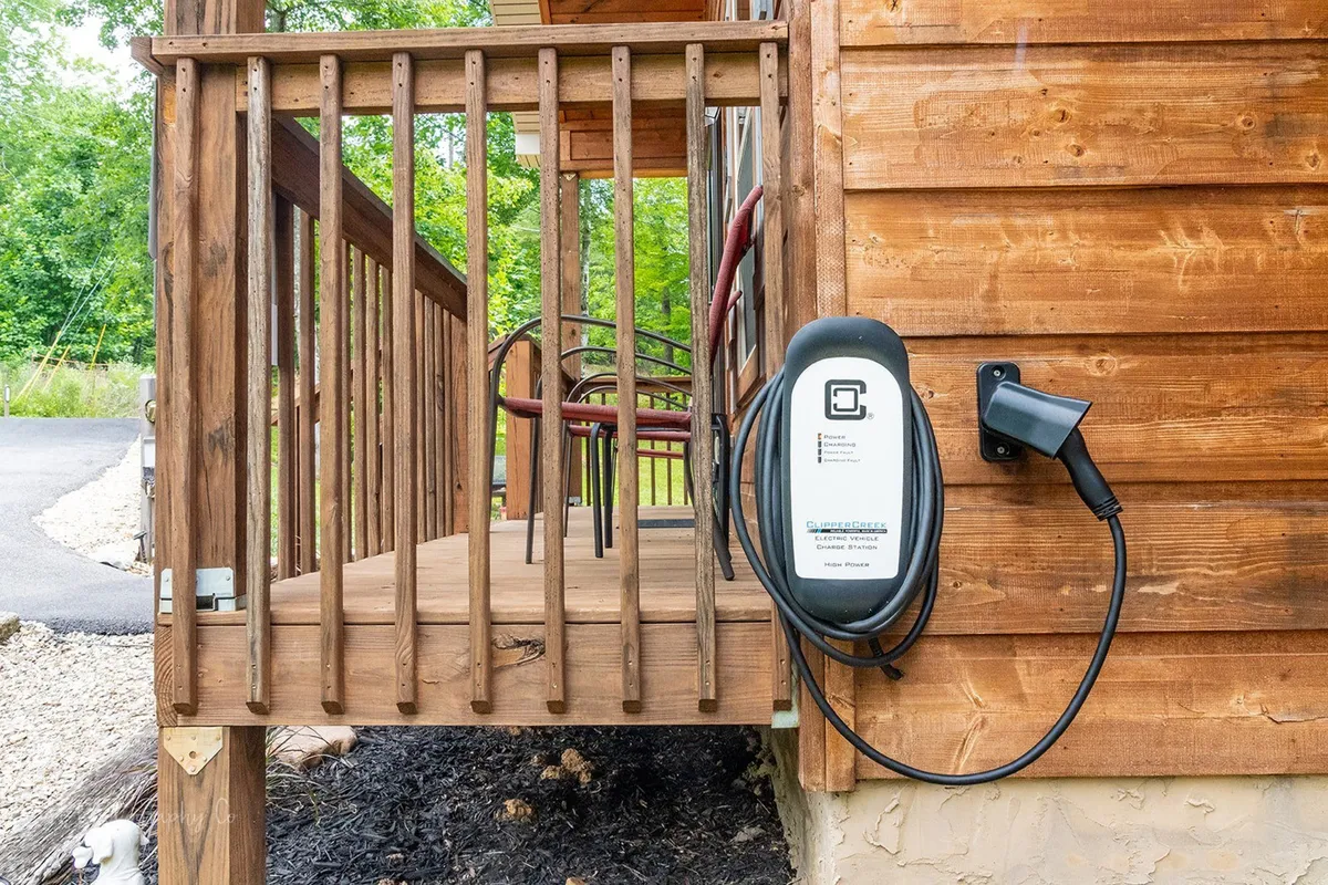 An exterior scene featuring an EV charging station next to wooden railings and outdoor seating, set against a backdrop of natural surroundings. The arrangement encourages both relaxation and eco-conscious travel.