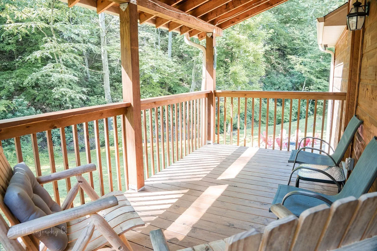 A cozy wooden deck with classic rocking chairs overlooks lush greenery, inviting guests to unwind while enjoying the peaceful sights and sounds of nature. The sturdy railing and wide deck boards convey a sense of safety and relaxation, while the natural surroundings hint at potential wildlife sightings.