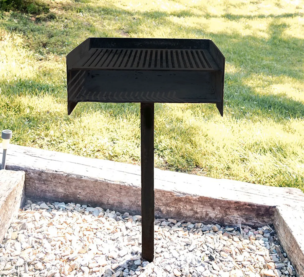 A standalone charcoal grill set atop a grassy lawn with a neat stone border, embracing a relaxed atmosphere perfect for outdoor cooking and social gatherings.