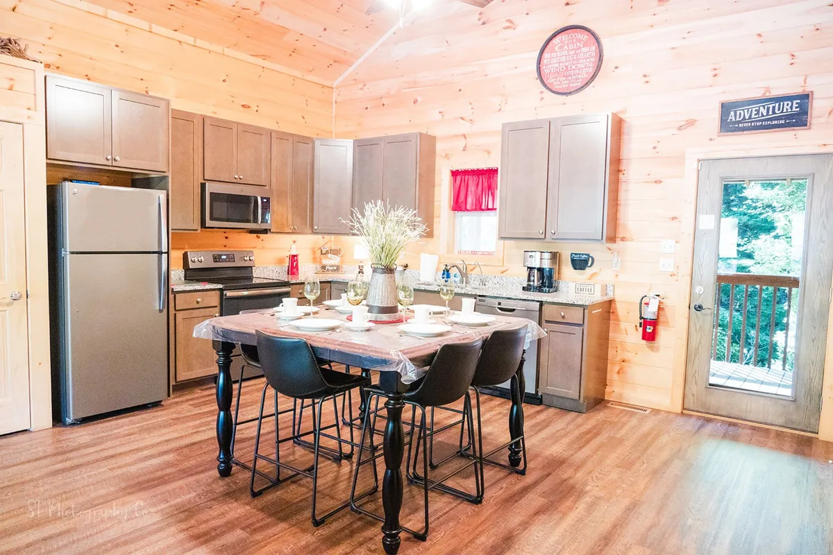 A spacious, open kitchen and dining area with a central dining table, a kitchen island featuring modern appliances, and a large window that lets in natural light. The setup is ideal for cooking and family meals, with enough space for social gatherings and group activities.