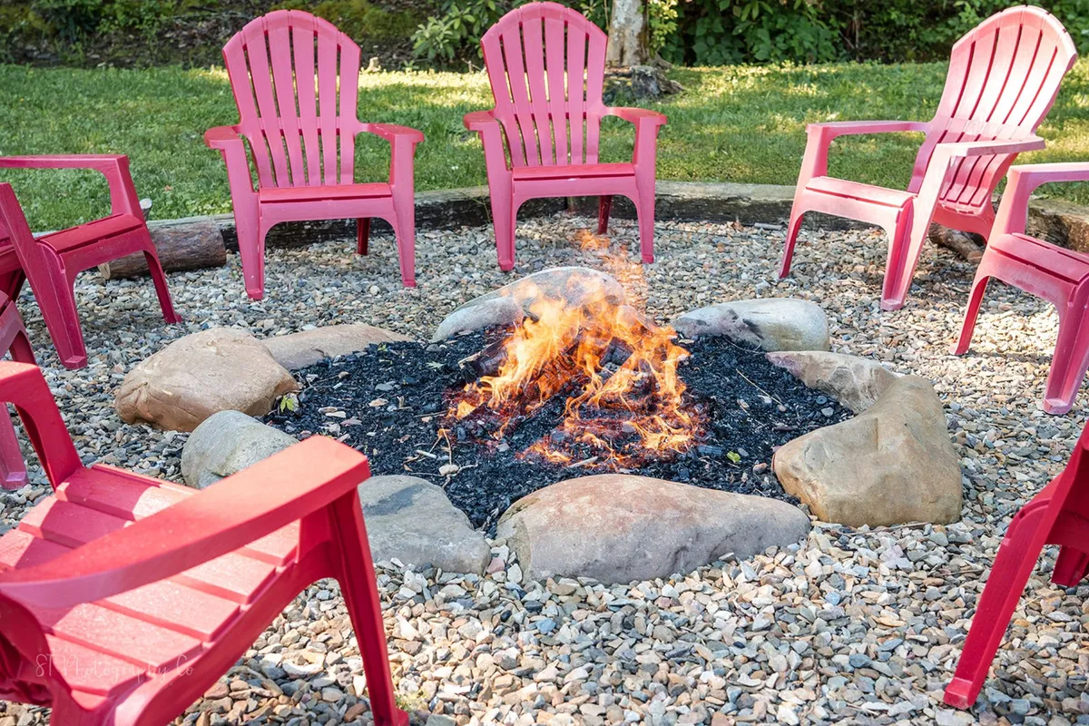A welcoming outdoor fire pit area surrounded by red chairs set amidst vibrant greenery. The fire pit creates a focal point for gatherings, ideal for storytelling, roasting s'mores, or stargazing after dark. The setup exudes a communal, inviting atmosphere for group relaxation and entertainment.