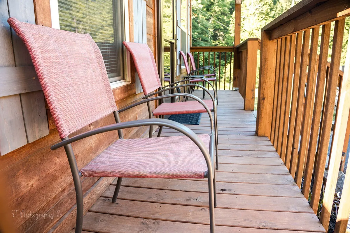 An exterior shot highlights a row of comfortable chairs lined up along a wooden deck railing, overlooking natural surroundings. The space is open and welcoming, with the deck suggesting a seamless indoor-outdoor connection and step-free access.