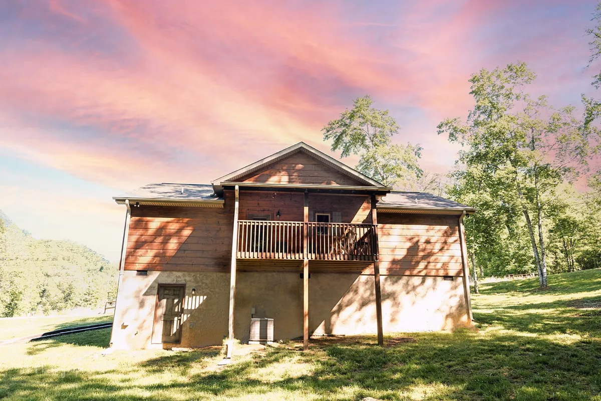 This inviting exterior shot features a wooden balcony nestled among greenery, with colorful clouds visible in the sky. The scene evokes a sense of peaceful seclusion and offers visual cues for access to nature trails and fresh outdoor experiences.